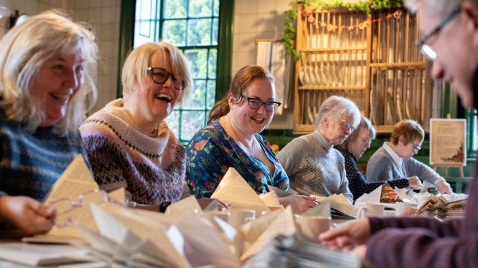 A row of people sat smiling at a table, with folded pages in front of them.